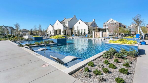 Pool area with in-water lounge chairs, lush planters, and elegant clubhouse.