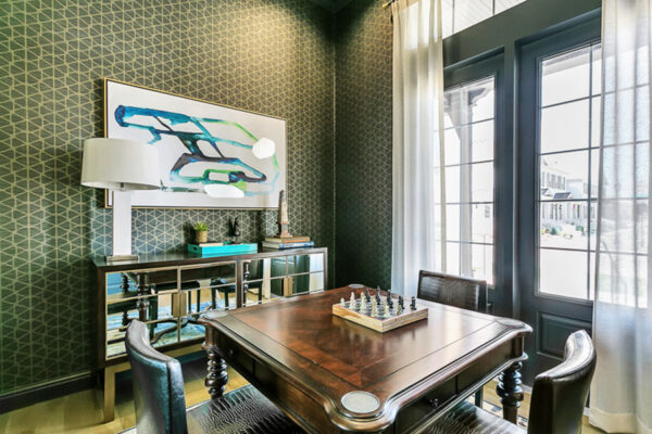 Elegant den with wood table, chess set, geometric wallpaper, and framed artwork.