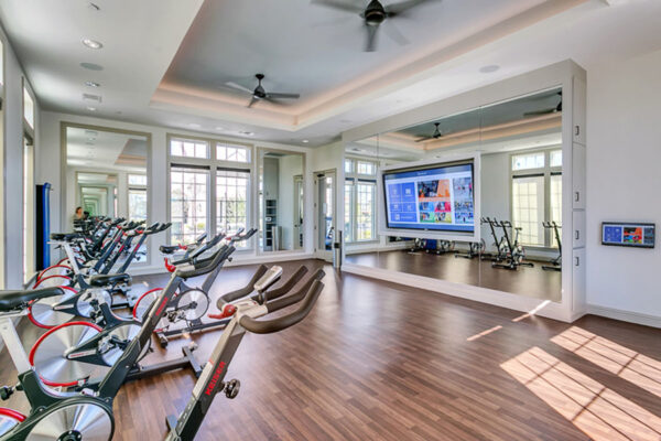 Spin room with wood style floor, mirror walls, spin bikes, and large TV.