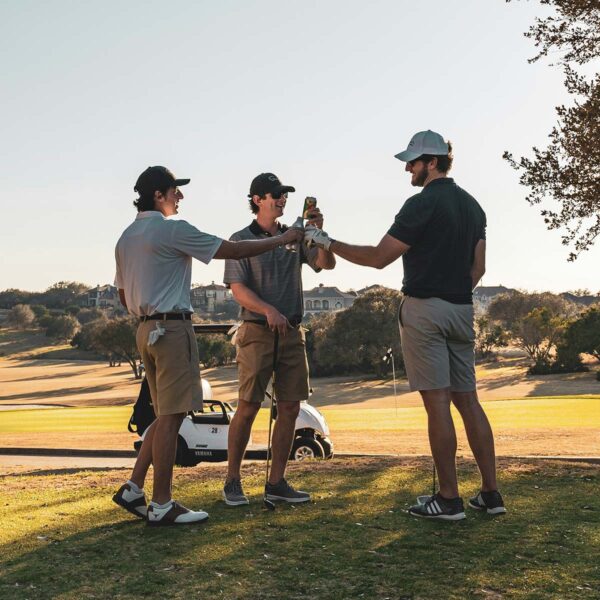 Friends toasting beers together on sunny golf course.