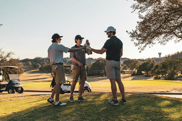 Friends toasting beers together on sunny golf course.